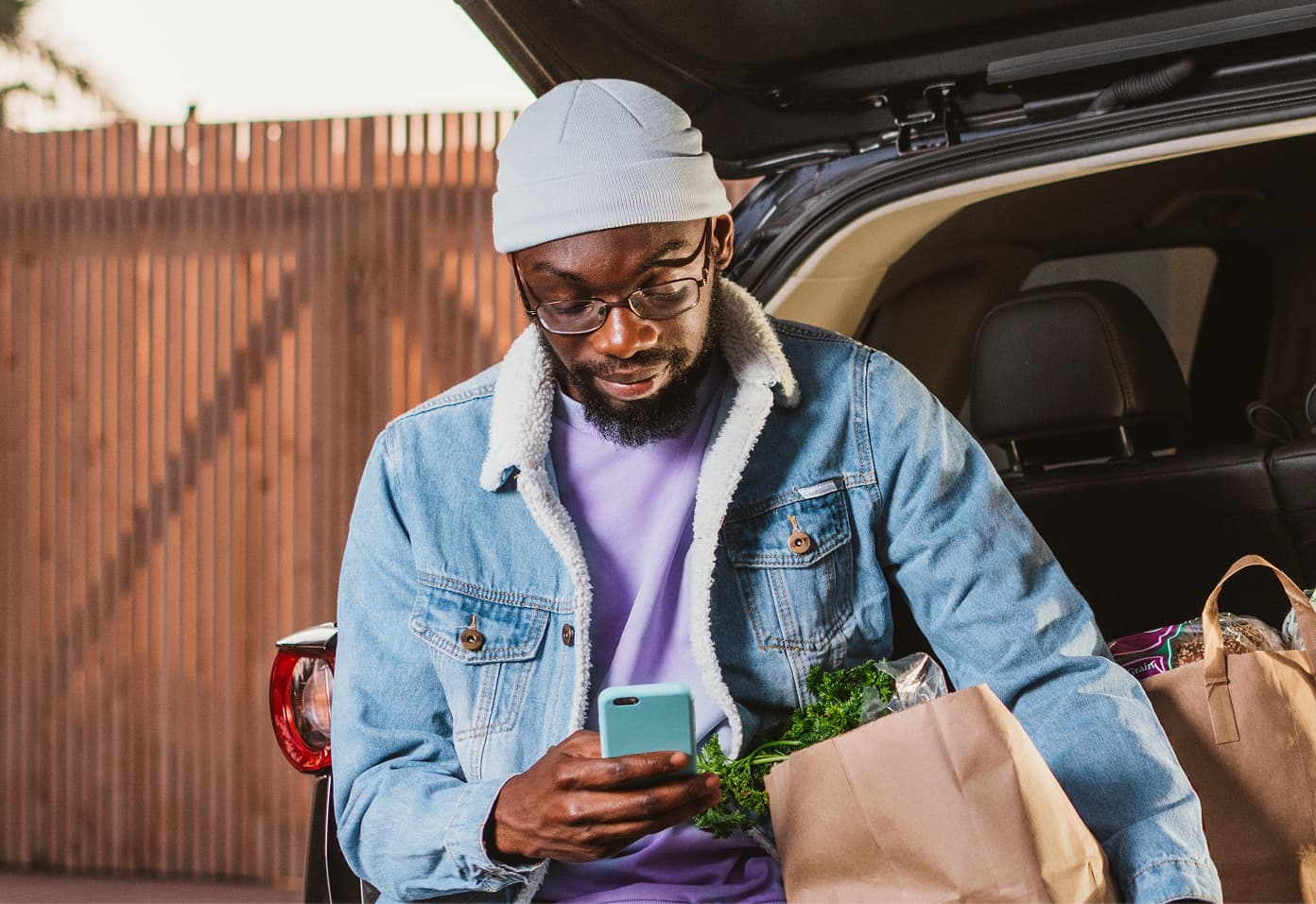 man in blue jean jacket and purple shirt checking phone for zelle money transfer (groceries)